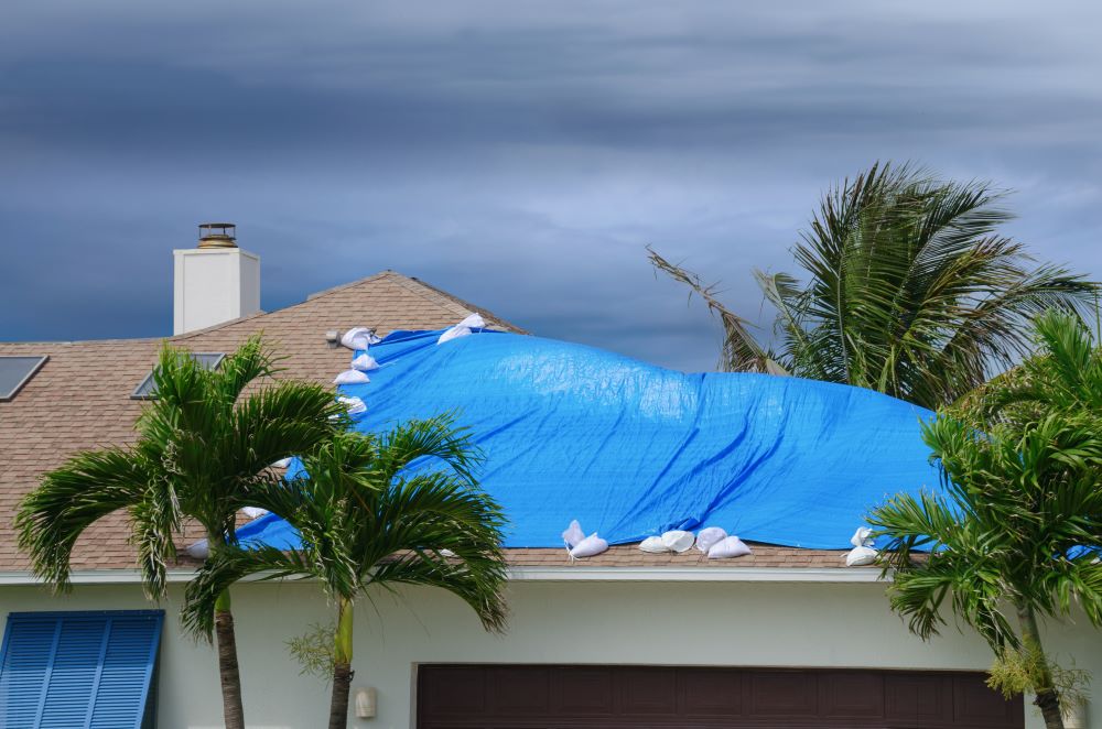 damaged roof covered by tarp as dark clouds approach
